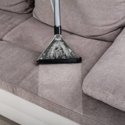 Closeup Of Woman Cleaning Sofa With Vacuum Cleaner At Home